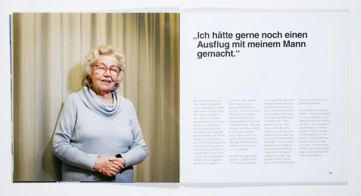 Older woman with gray hair, glasses, and light-blue sweater smiles softly beside beige curtains; right page shows a German quote in a magazine spread.