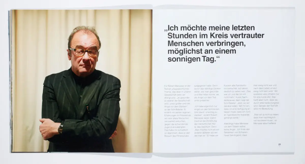 Older man in a pinstriped suit and glasses, arms crossed, stands before a beige curtain; opposite page features a large German quote.