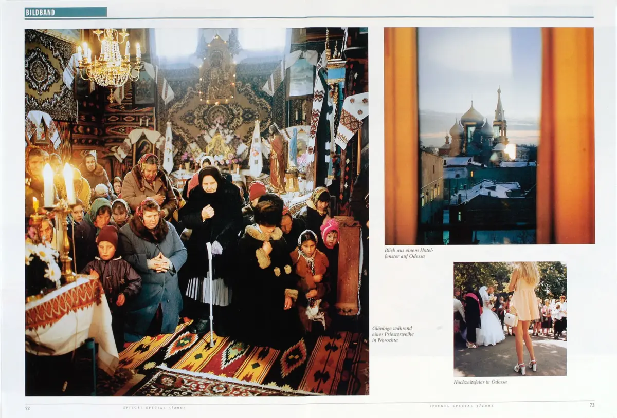 Crowded Orthodox church worshipers praying among icons, candles, and woven textiles.