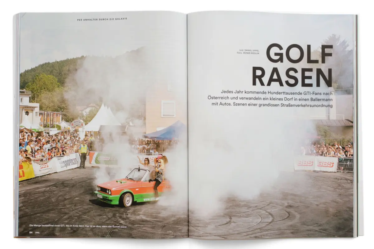 Volkswagen GTI race car speeds through a smoky street rally as crowds line the barriers.