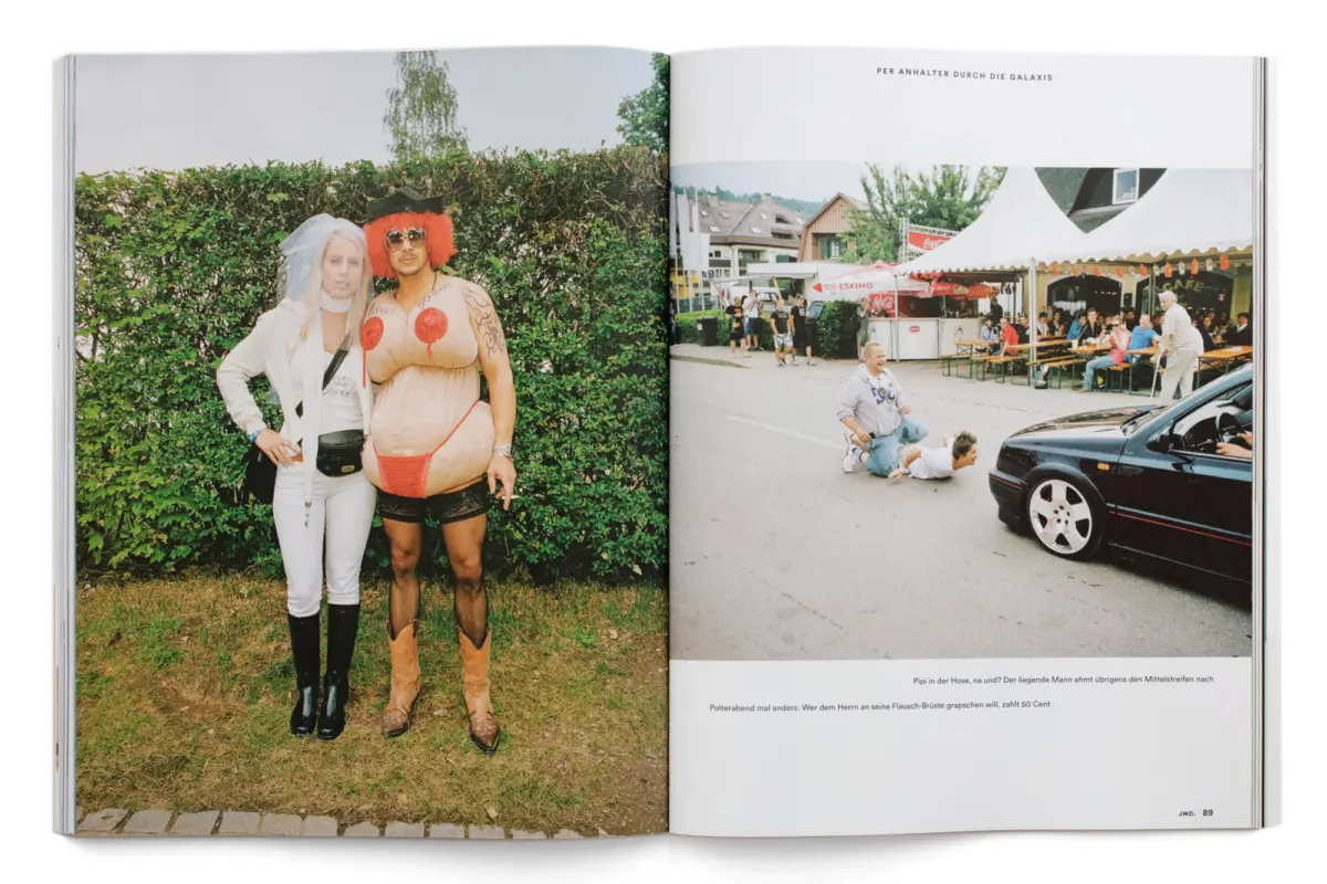 Two costumed individuals pose by a hedge; one in white bridal outfit with veil, the other in orange afro wig and inflatable bodysuit; festival crowd.