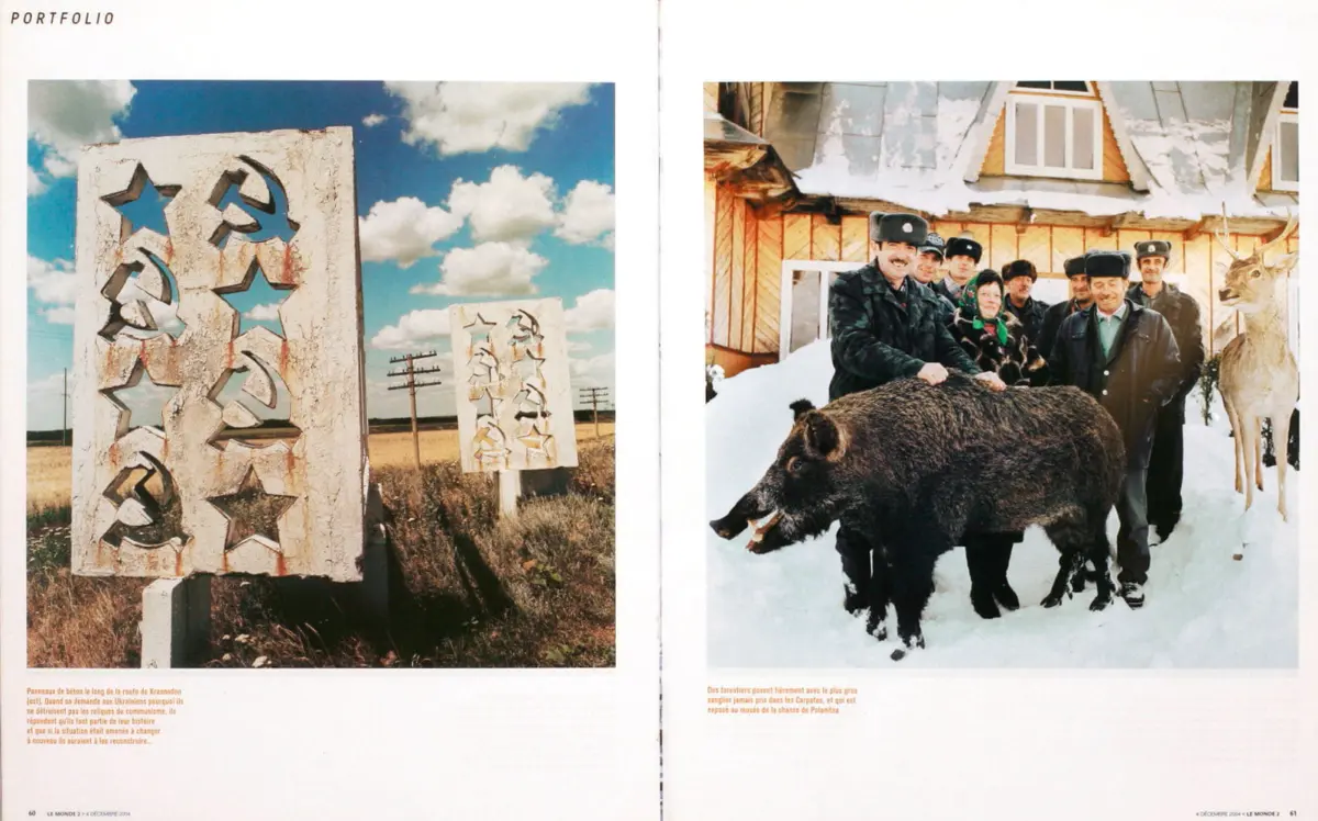 Cracked concrete monument panels with star and hammer-and-sickle cutouts in a rural field under a blue sky.
Group of foresters in winter coats pose with a large boar in the snow outside a wooden house.