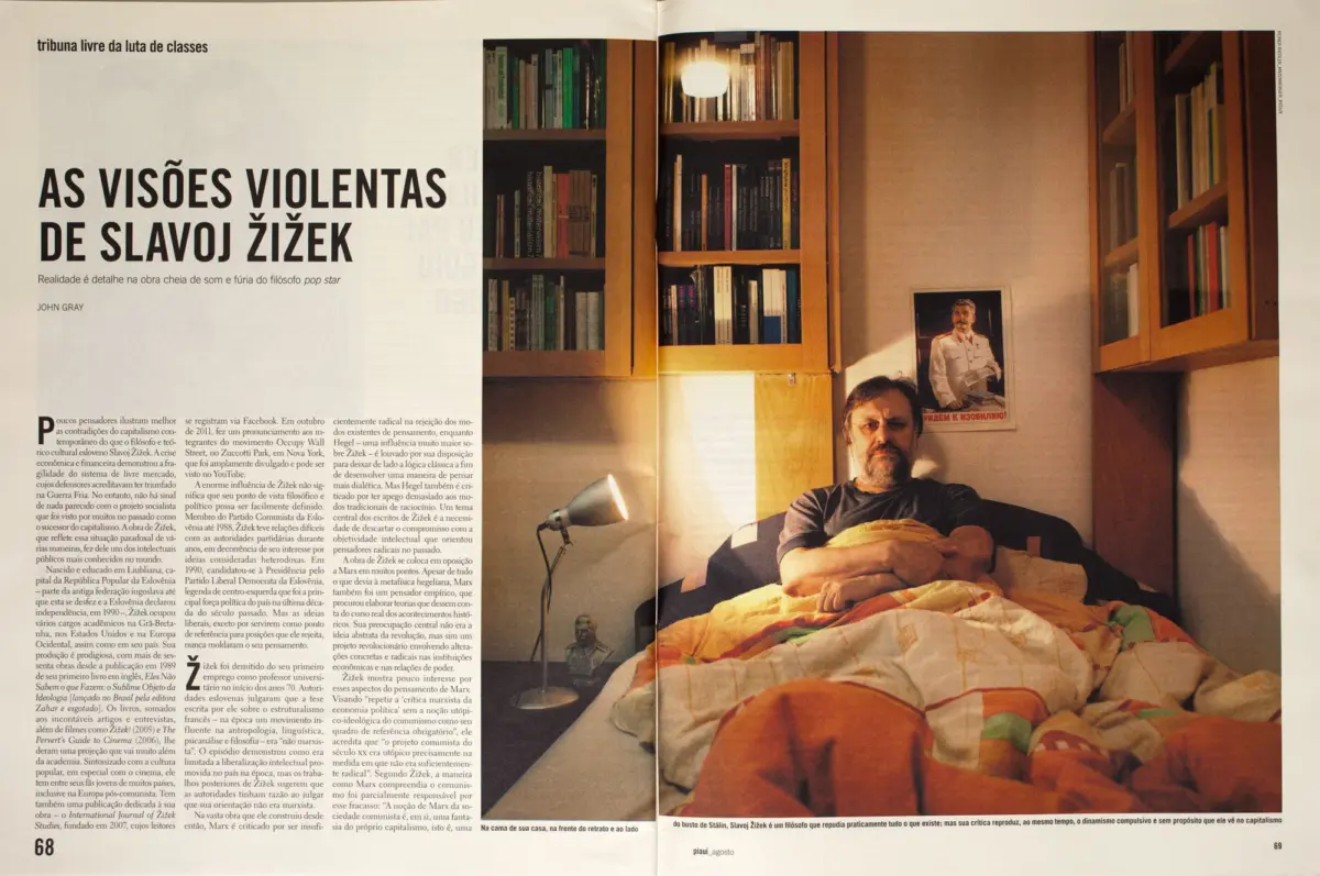 Bearded man reclining on a bed in a bedroom with tall wooden bookshelves, a framed poster of a man in a white uniform, and a colorful quilt.