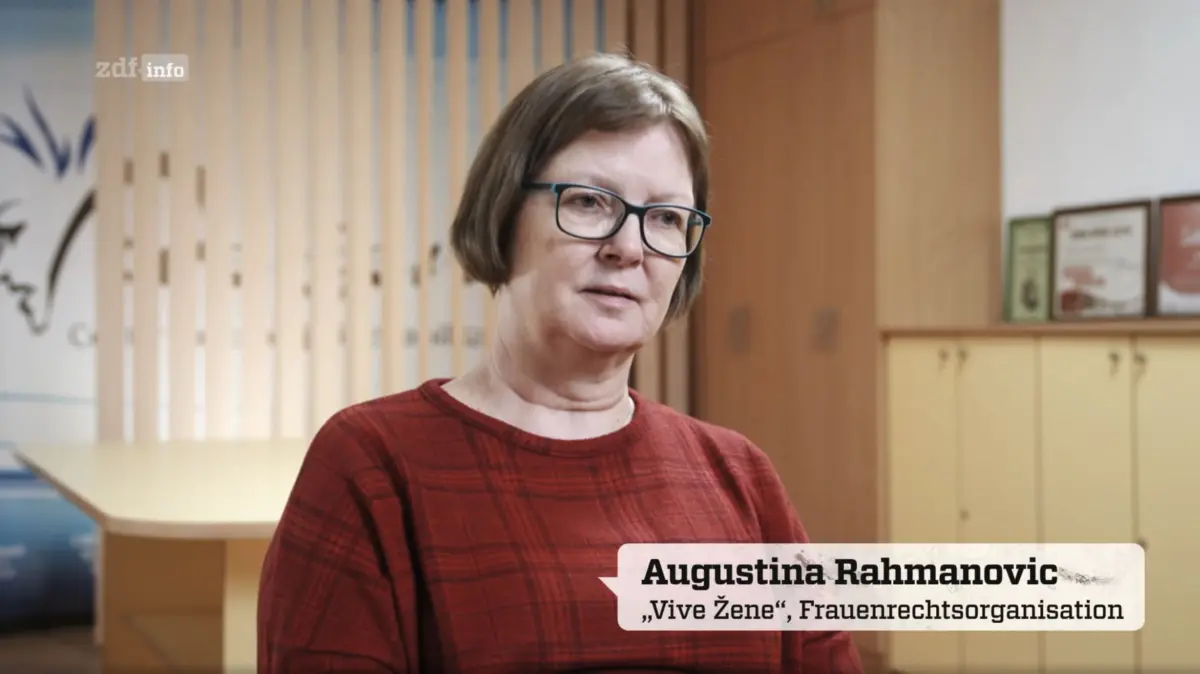 Portrait of Augustina Rahmanovic speaking in an office with wood slat backdrop and framed awards.