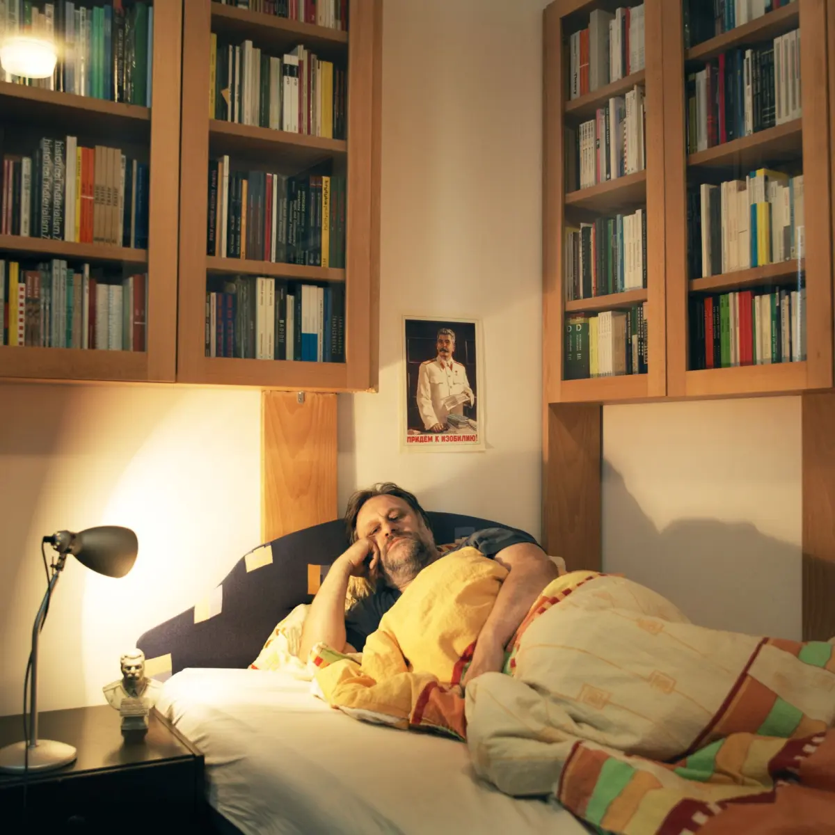 Adult person lying in bed with hand on face in a wood bookcase-lined bedroom.