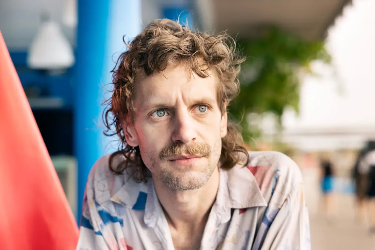 Man with brown curly hair and mustache gazes upward at an outdoor playground.