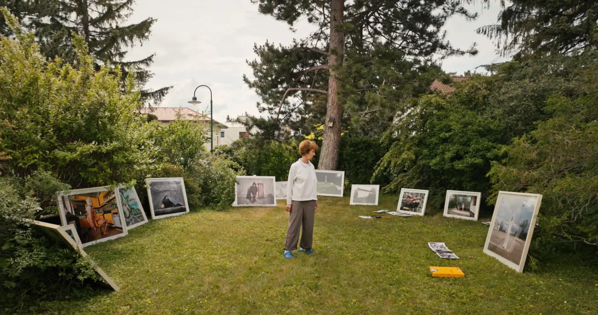 Older adult in a garden examining large framed photographs arranged on the grass.