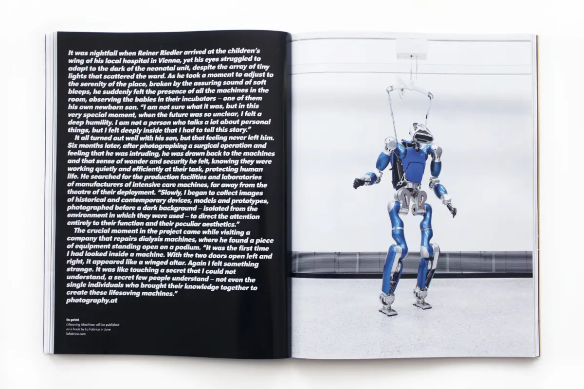 Open two-page spread: left page black with white text; right page blue humanoid robot suspended by overhead hoist in a studio.