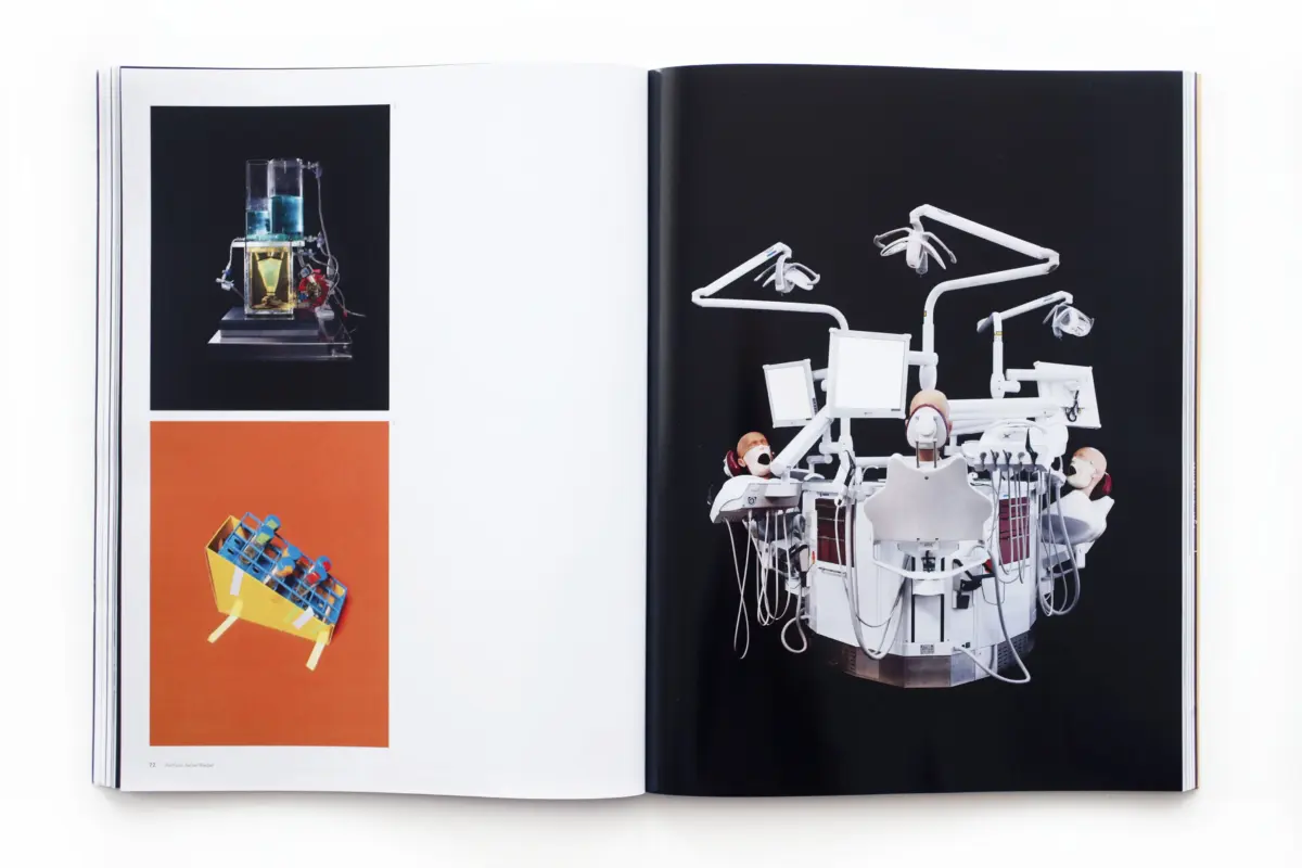 Open book shows a white dental chair with multiple arms on a black page; page features glass lab apparatus and a yellow wheelbarrow with blue blocks.