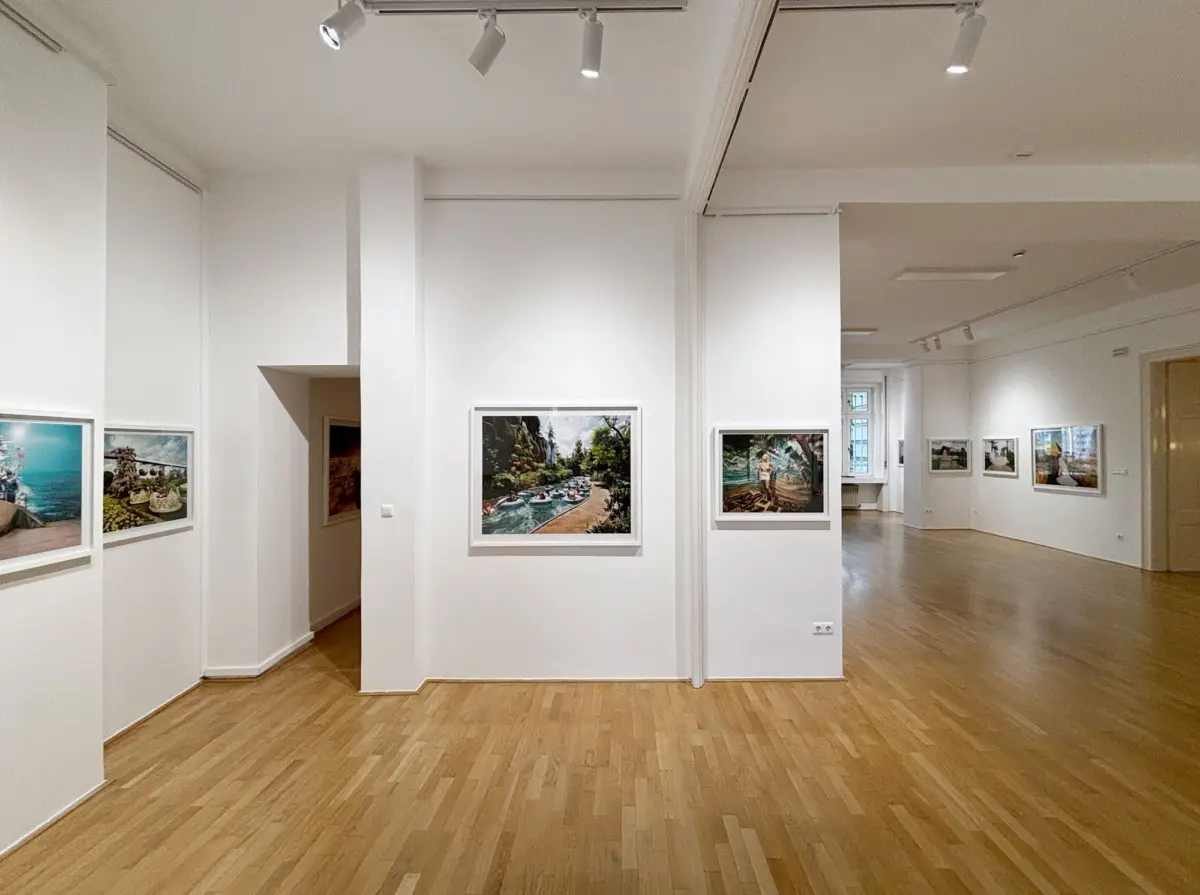 Art gallery interior with white walls, wooden floor, and framed landscape photographs on display under track lighting.