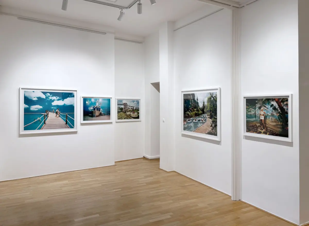 Art gallery interior with framed landscape photographs on white walls and a light wooden floor.
