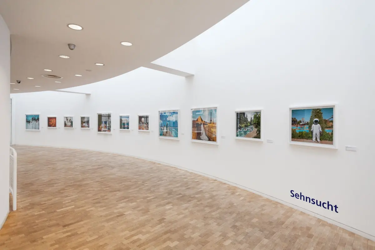 Art gallery interior with white curved ceiling, recessed lights, and a row of framed photographs along the wall.