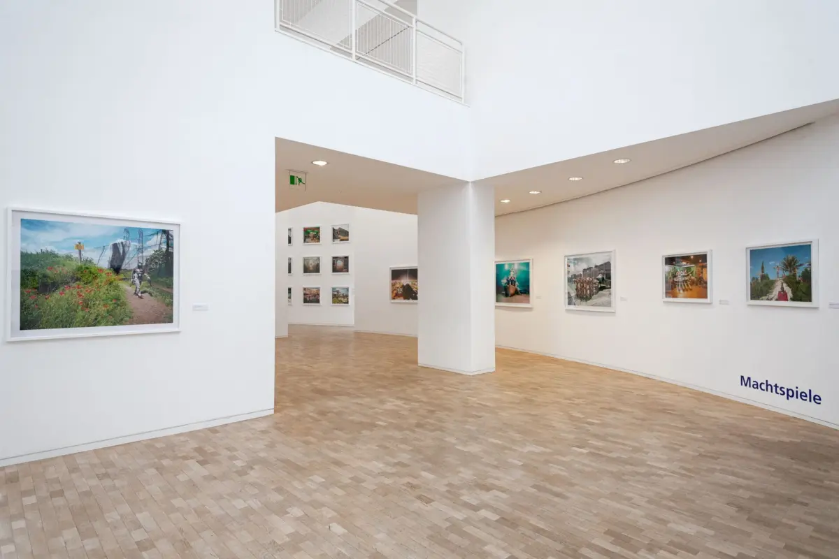 Bright white art gallery interior with framed photographs on white walls and a beige tiled floor.