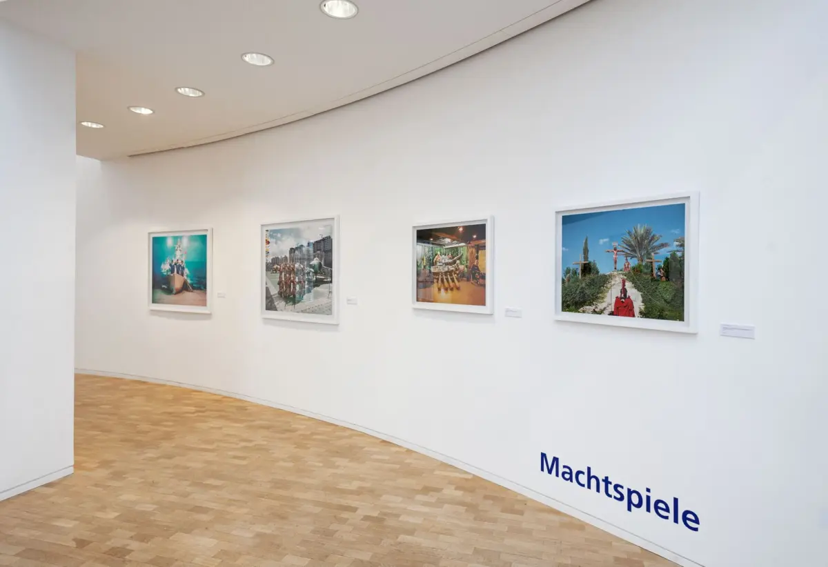 Four framed photographs displayed along a curved white gallery wall with recessed ceiling lights and a wooden floor.