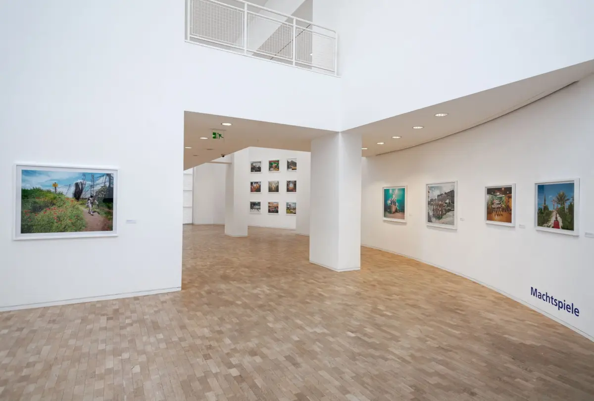 Spacious white-walled art gallery interior with wooden floor and framed photographs on the walls.