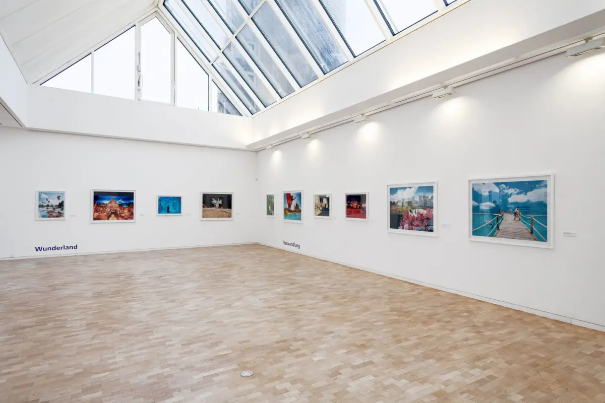 Bright contemporary art gallery interior with white walls, skylight ceiling, and framed photographs along the walls.