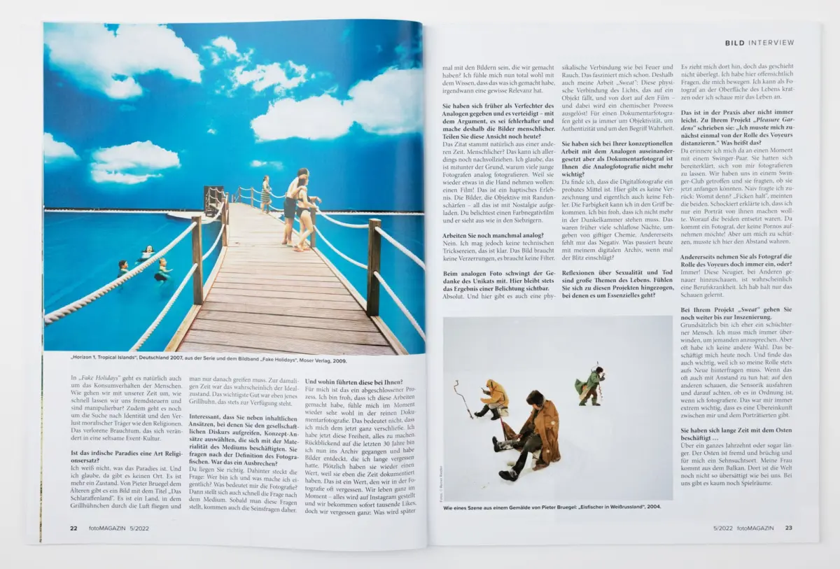 Wooden pier extends into turquoise sea; people in swimsuits walk along the deck under a blue sky.