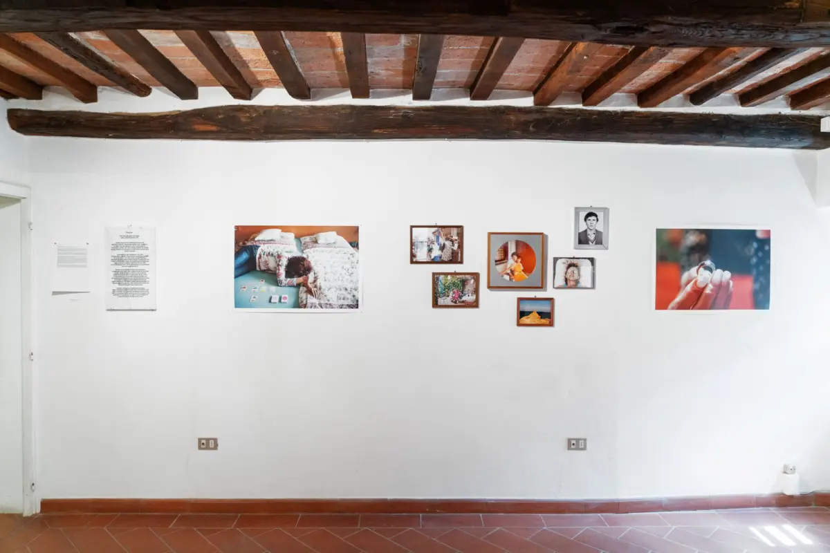 Interior gallery wall with assorted framed photographs and documents under exposed dark wooden beams and terracotta tile floor.
