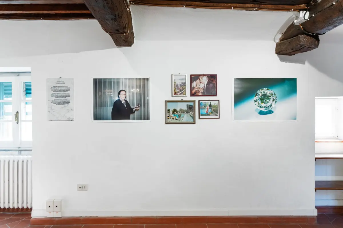 Interior of an art gallery with white walls, exposed wooden ceiling beams, and framed photographs; a large diamond artwork on the right wall.