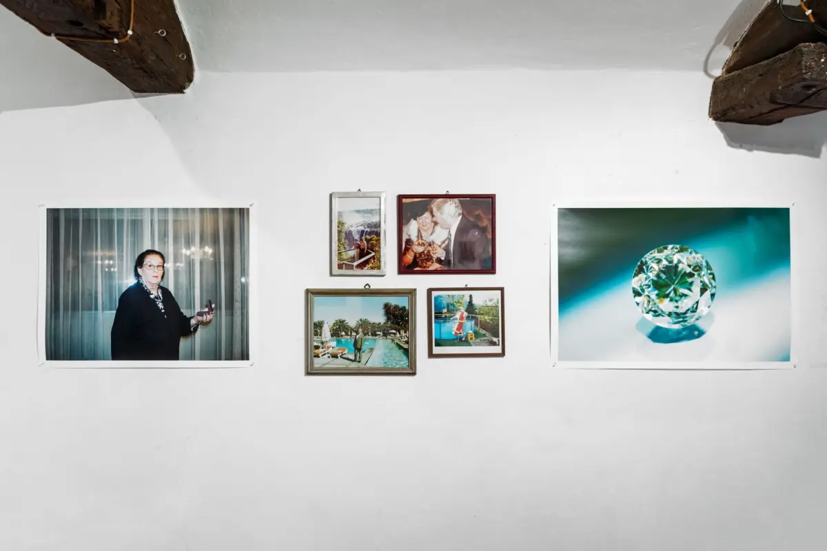 Adult person stands beside a large framed portrait on a white gallery wall, with several smaller frames and a blue diamond artwork.