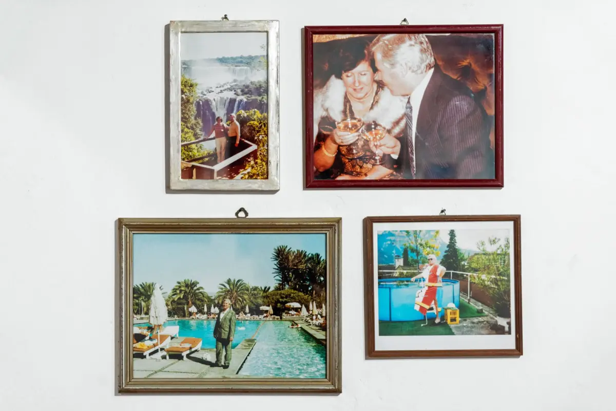 Wall with four framed travel photos: two people at a waterfall overlook; a couple toasting; two poolside scenes.