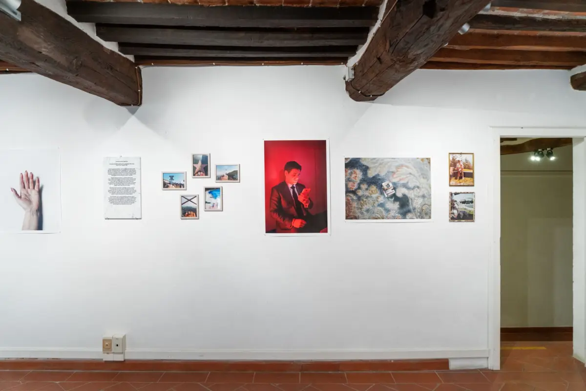 Art gallery wall with multiple framed photos, featuring a large red portrait of a man in a suit checking his phone; exposed wooden ceiling beams.