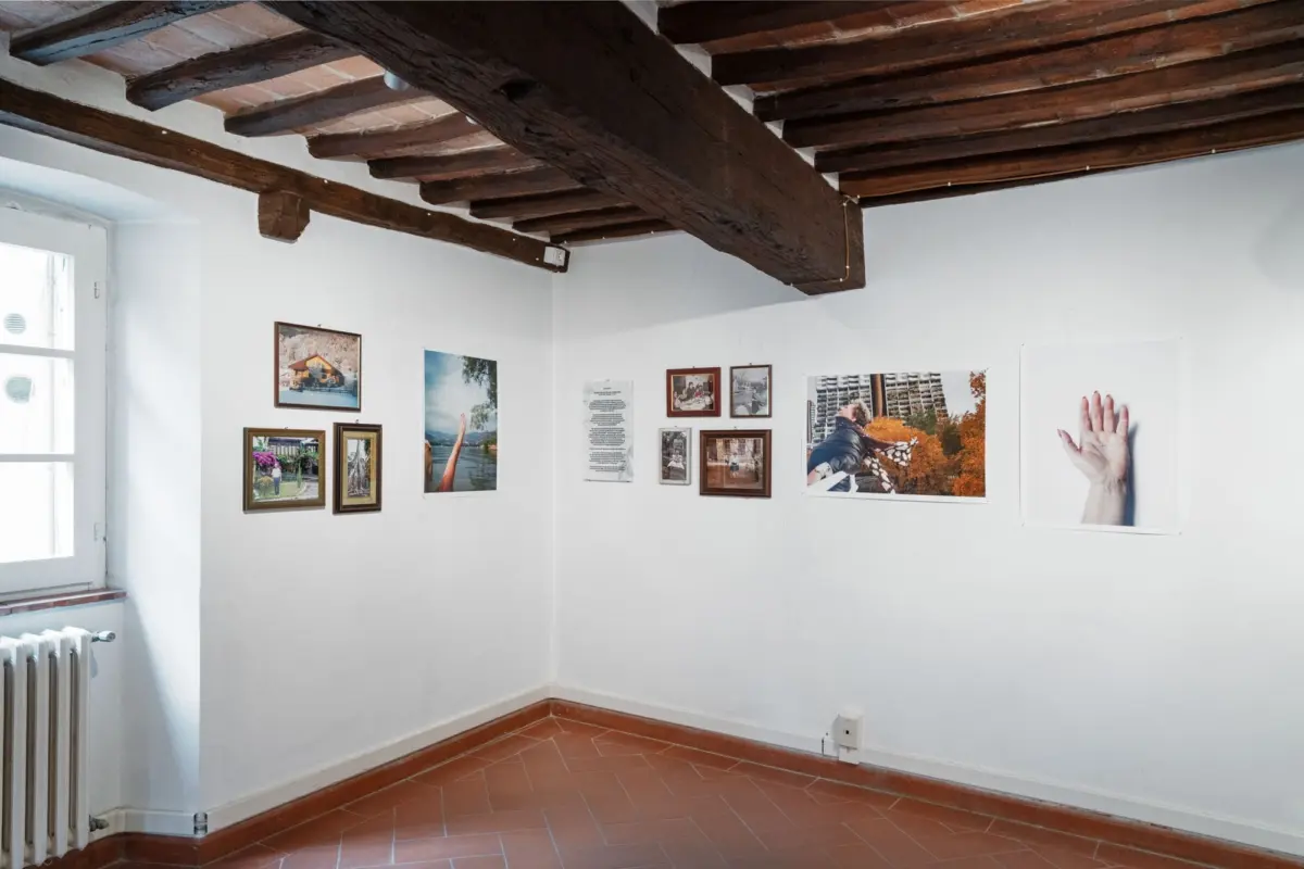Gallery corner with white walls, exposed dark wooden ceiling beams, framed photographs, and a large hand image on the wall.