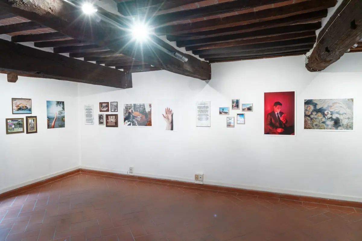 Gallery interior with white walls, exposed dark wooden beams, and framed artworks along the wall, including a large red portrait on the right.