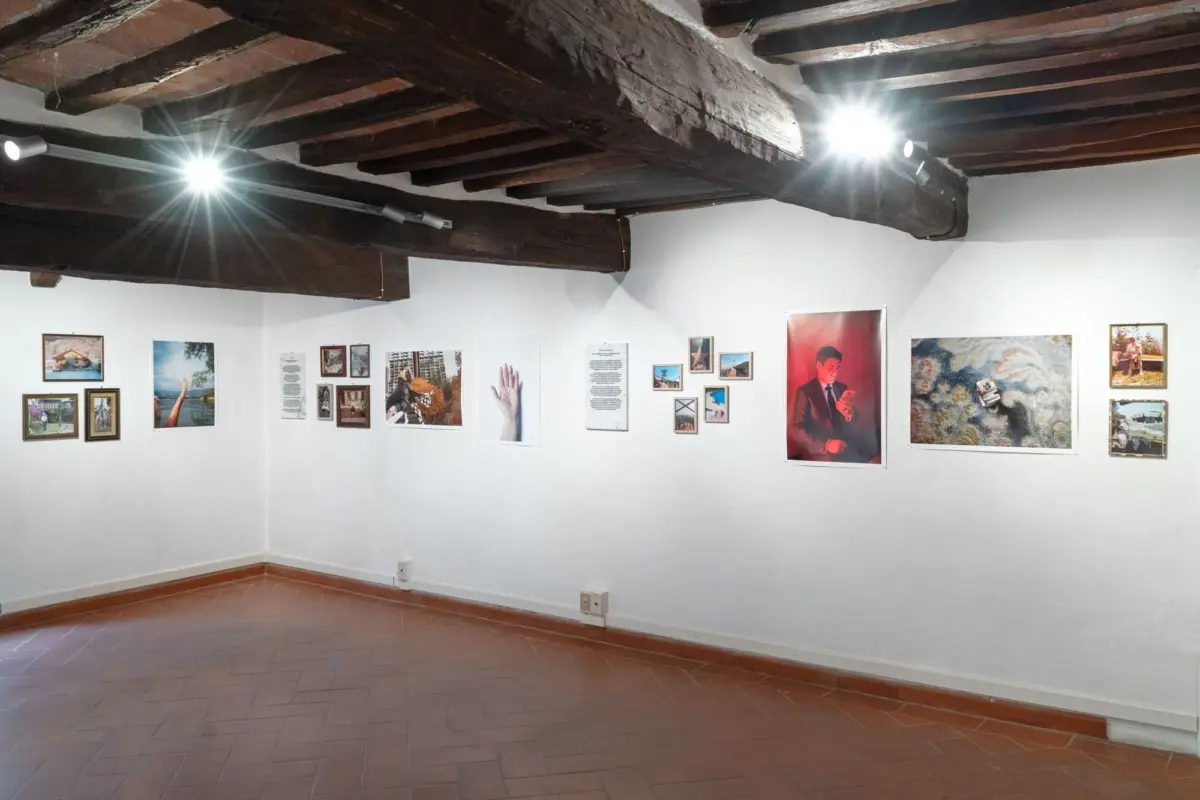 Interior of an art gallery featuring exposed wooden ceiling beams, track lighting, and a wall with framed photographs and posters.