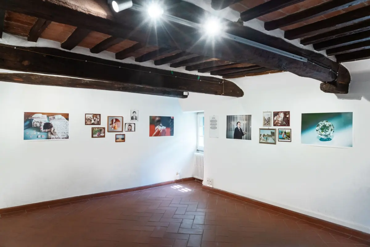 Gallery interior with white walls, dark exposed timber beams, and framed photographs; terracotta tile floor.