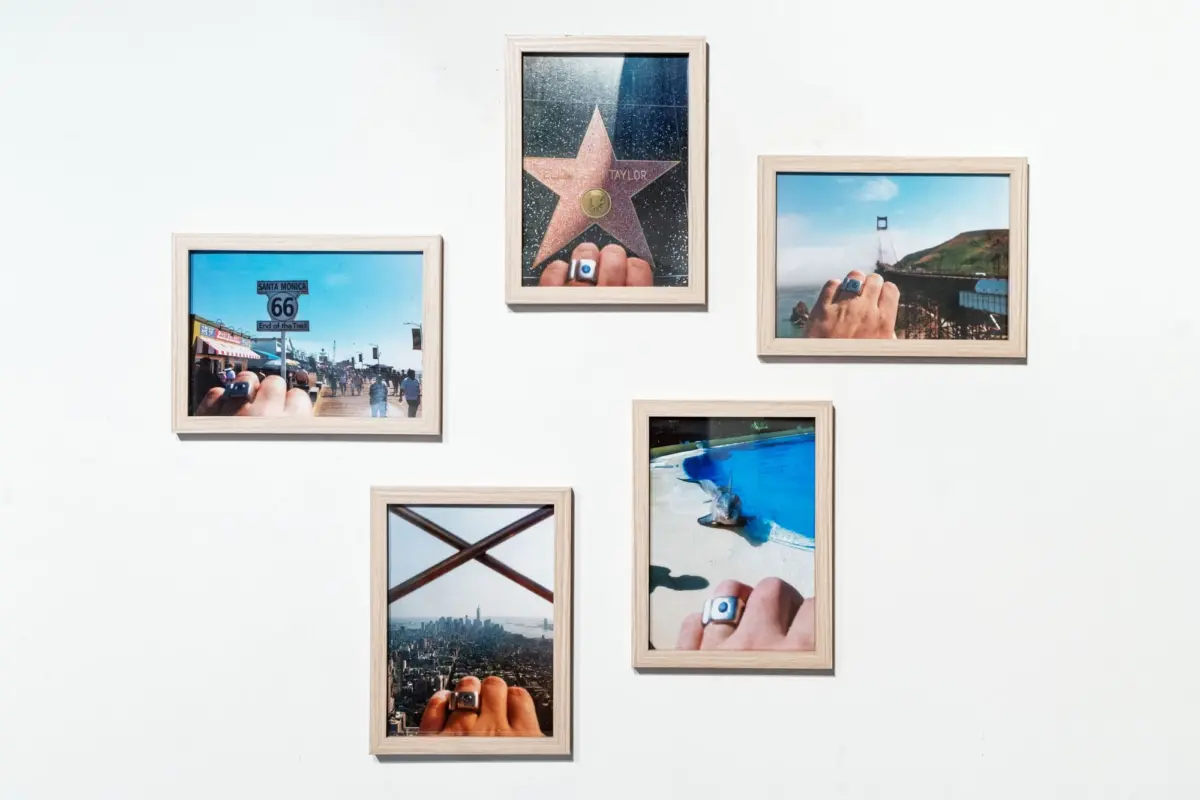 Wall display of wooden-framed travel photos showing hands with rings, including Route 66 sign, Walk of Fame star, Golden Gate Bridge, and beach.