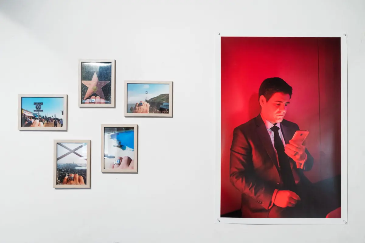 Gallery wall with small framed photos; large red-lit portrait of a suited person looking at a smartphone.