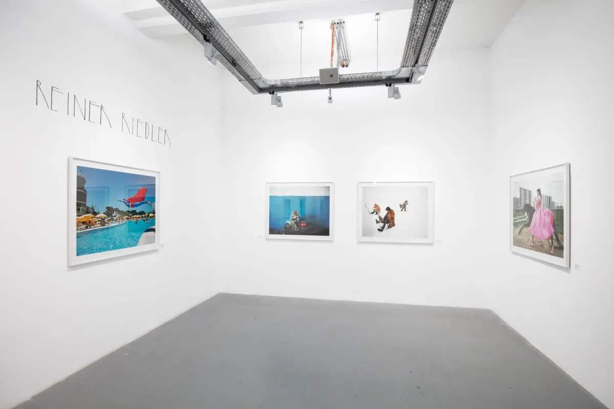 White-walled gallery with five framed photographs; overhead metal track lighting; left wall displays the name REINER NIEDLER.