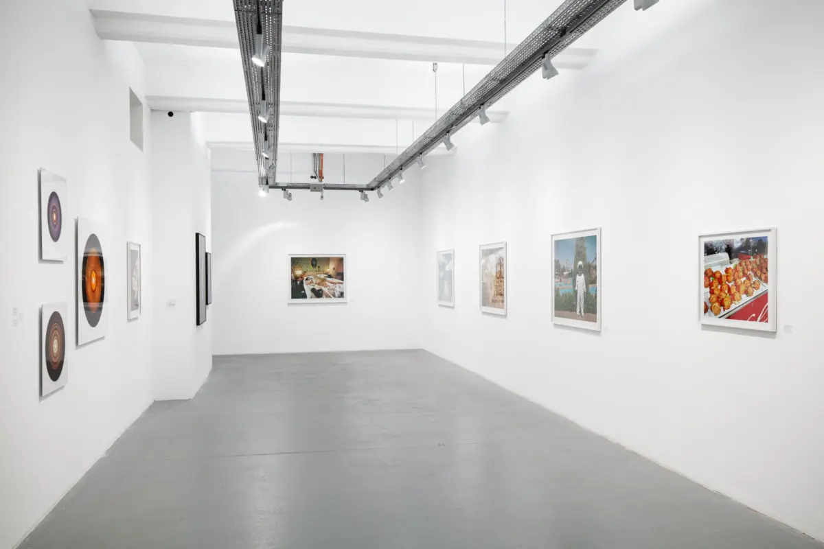 Empty white-walled art gallery with framed photographs along the walls and overhead track lighting.