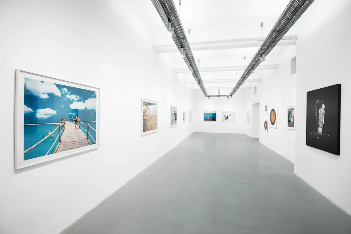 White-walled art gallery corridor lined with framed photographs under overhead track lighting.