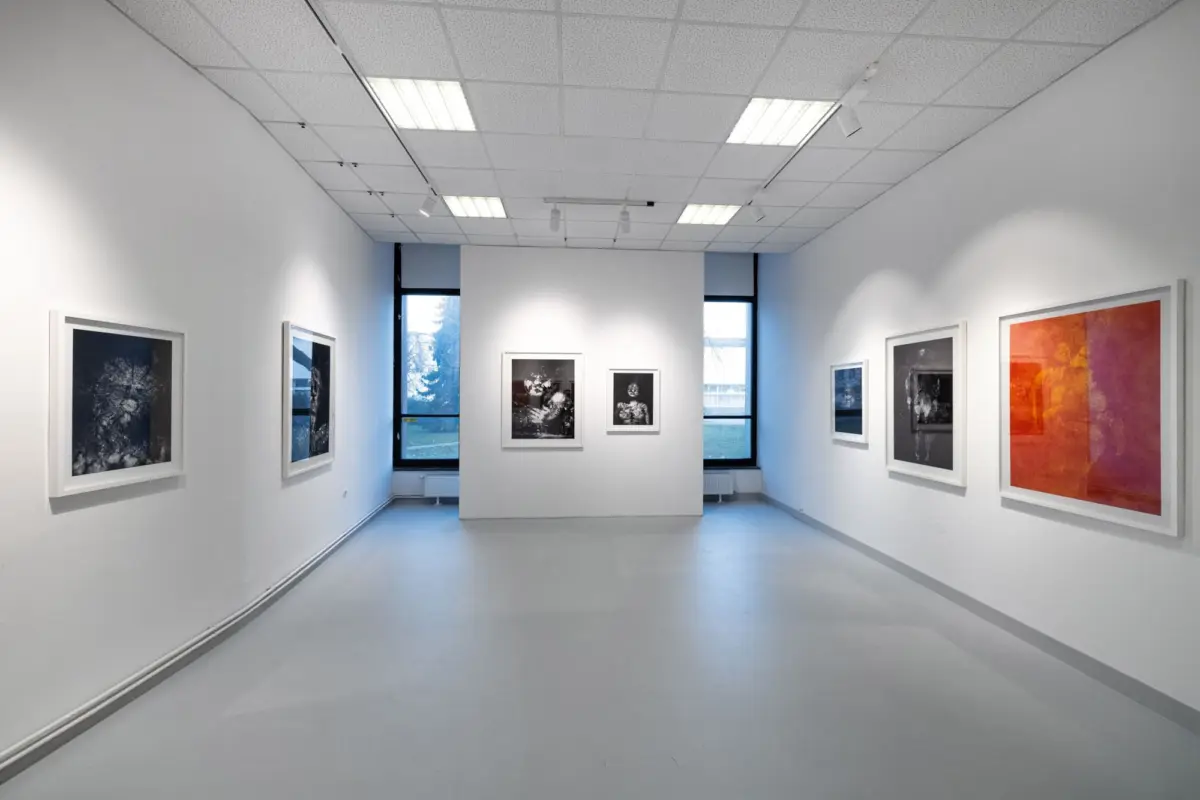 Wide gallery interior with white walls, framed black-and-white photographs along both sides, and windows at the far end.