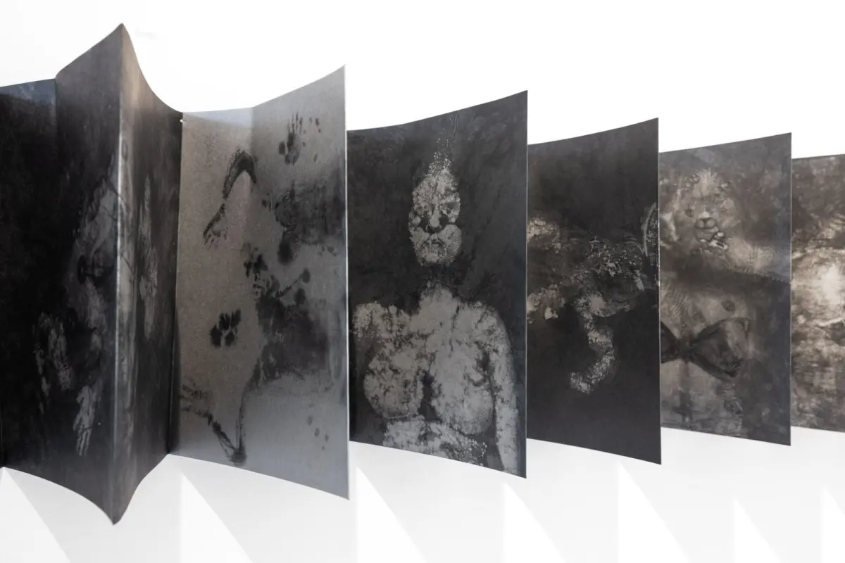 Row of tall, dark exhibition panels with textured prints, arranged in a wave along a white gallery floor.