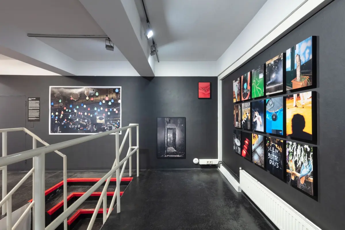 Gallery corridor with a grid of photographs on the right and a red-edged staircase on the left beneath track lighting.