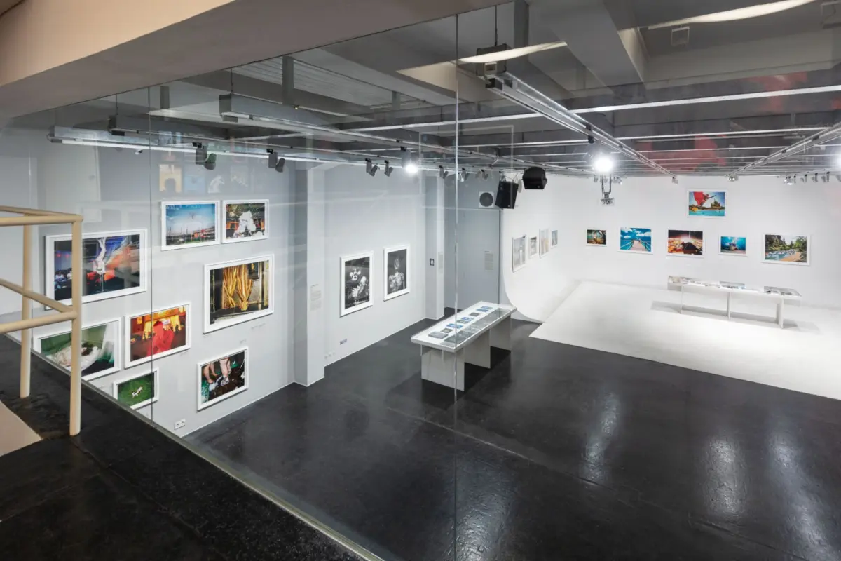 Contemporary art gallery displaying framed photographs on white walls, with glass partition and central display tables.