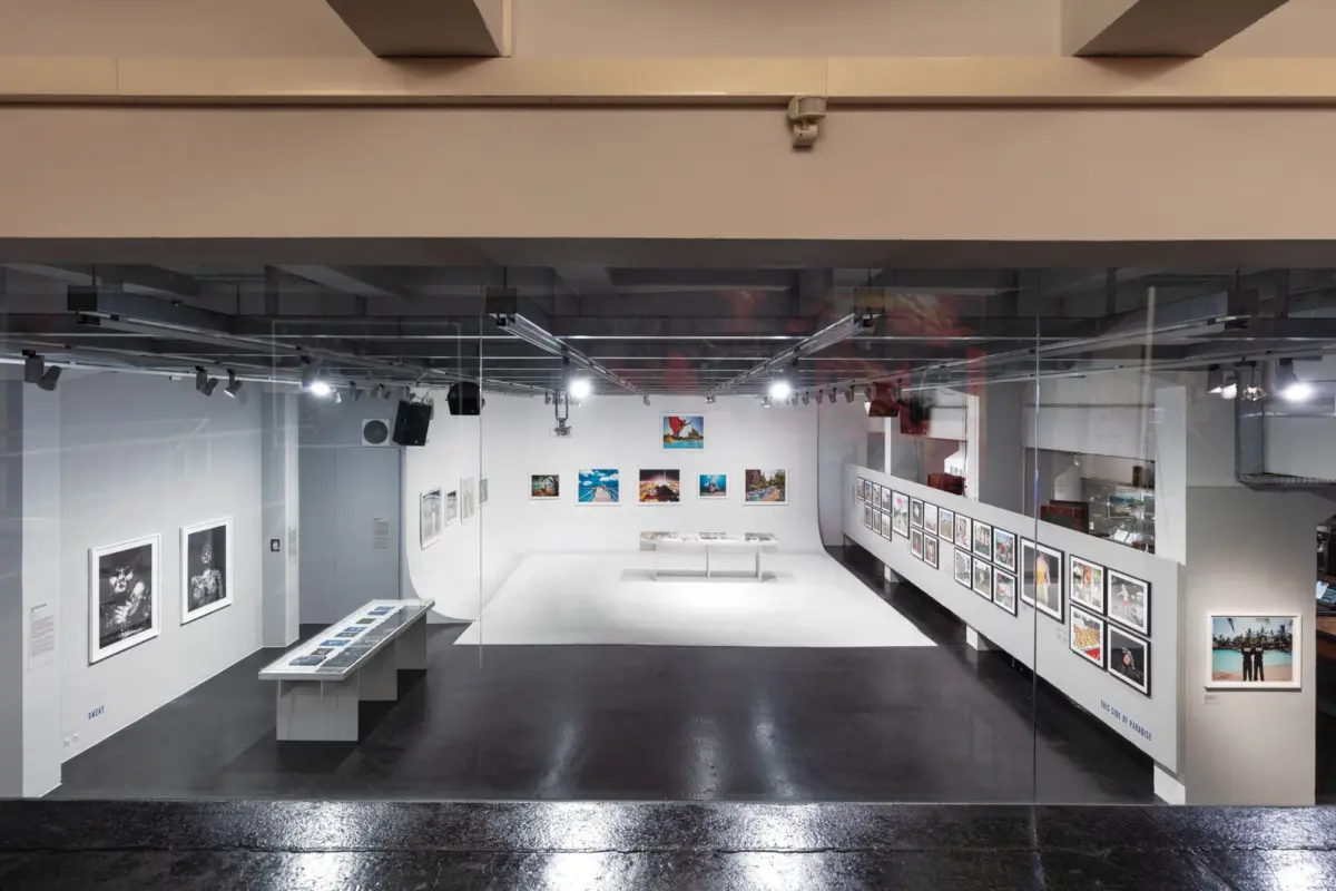 Empty contemporary art gallery interior with glass partitions and numerous framed photographs on white walls.