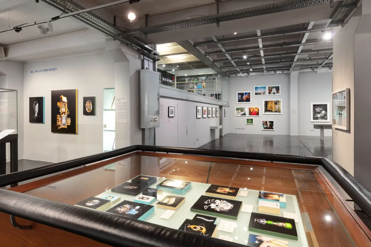 Modern art gallery interior with framed photographs on walls and a glass-topped display case in the foreground.
