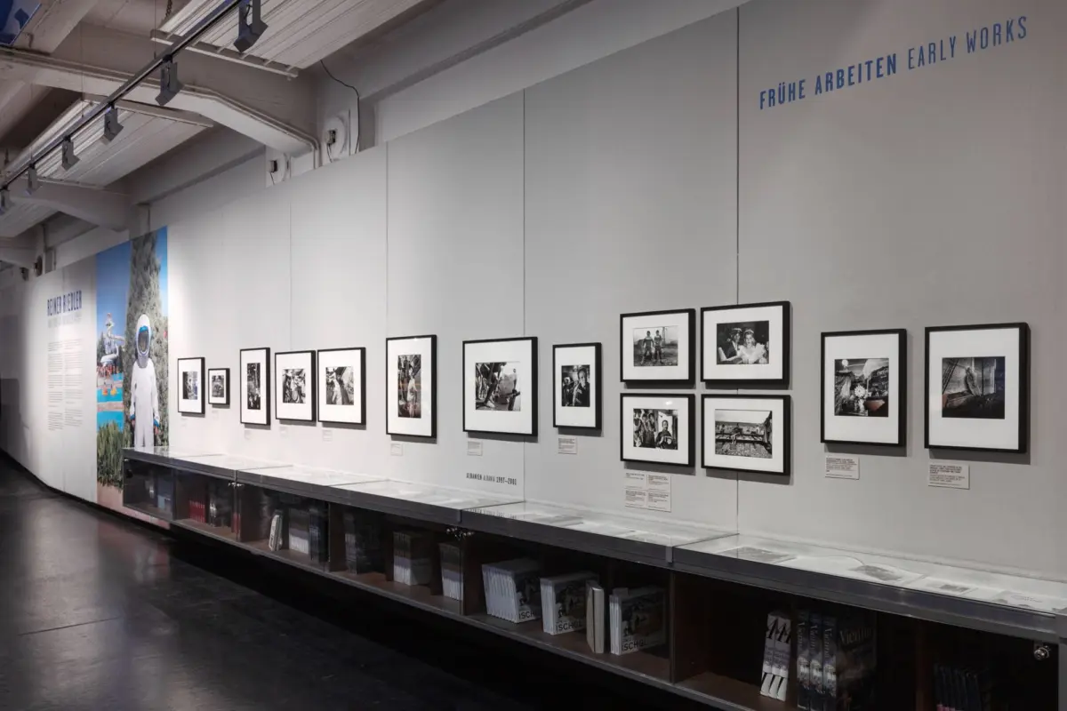 Gallery wall of black-and-white framed photos in a row, gray wall, glass display case beneath, and a large blue poster with an astronaut on the left.