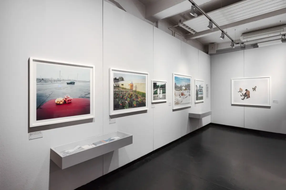 Framed photographs displayed along white gallery walls under track lighting in an art gallery.