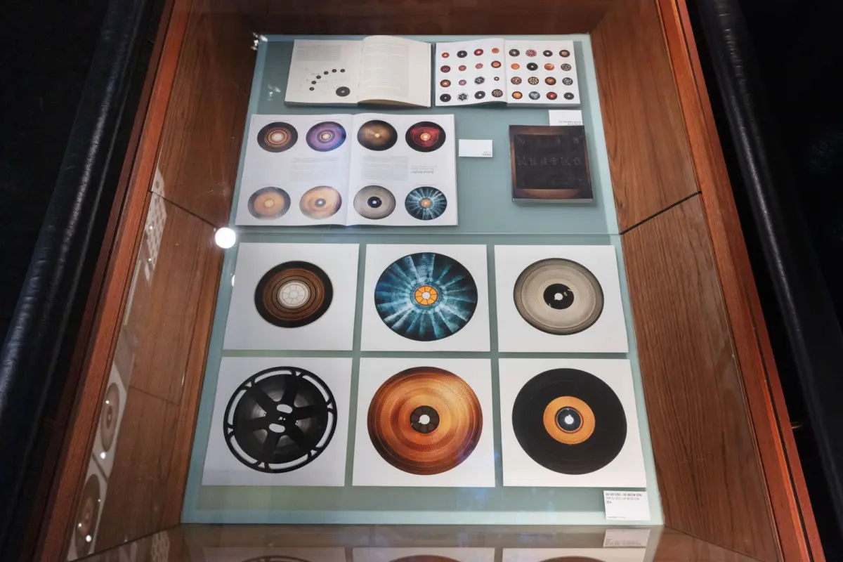 Glass-fronted display case showcasing open books and circular disc illustrations on a blue surface.