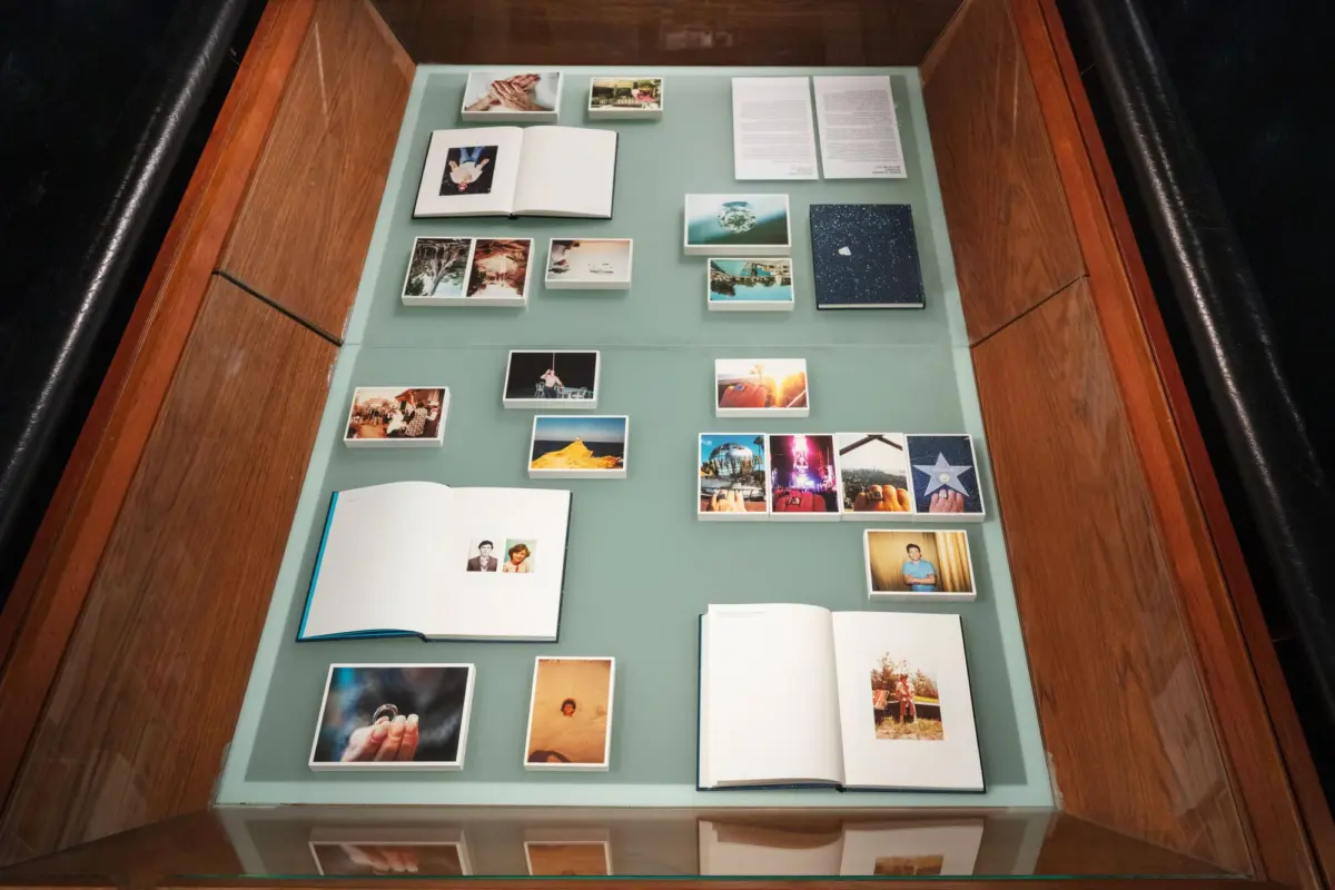 Glass-topped display case displaying an open photo album and numerous small photographs in white frames on a green display board.