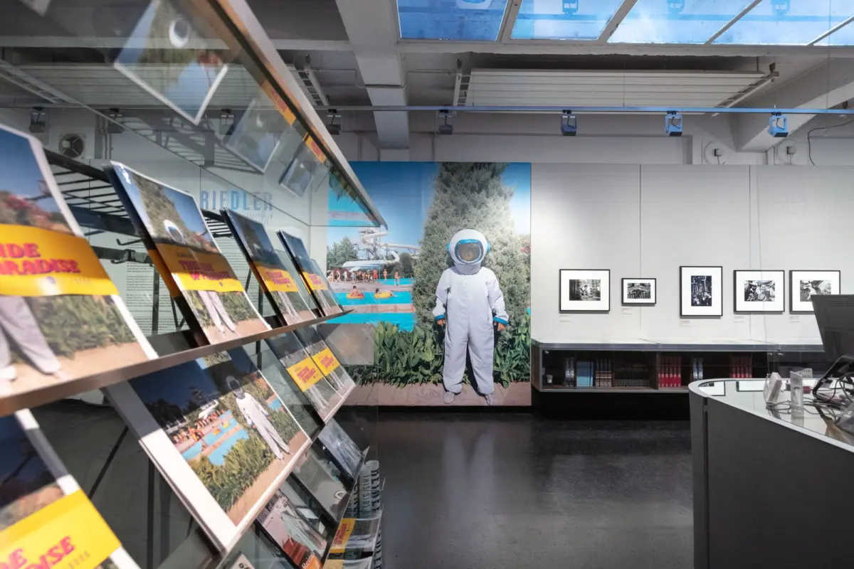 Life-size astronaut in a white spacesuit standing in a modern museum gallery with angled display boards and framed photos.