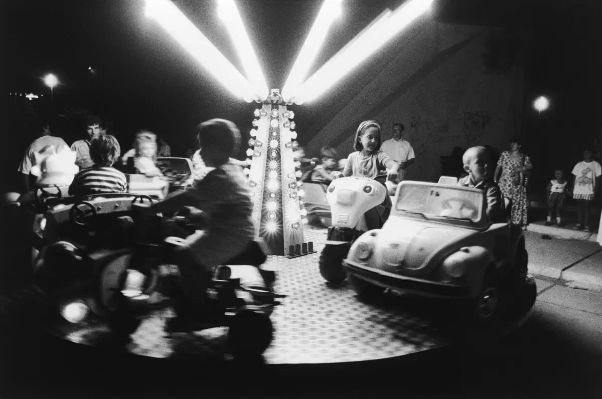 Riders in bumper cars circle a tall, brightly lit central pillar at an indoor amusement park.