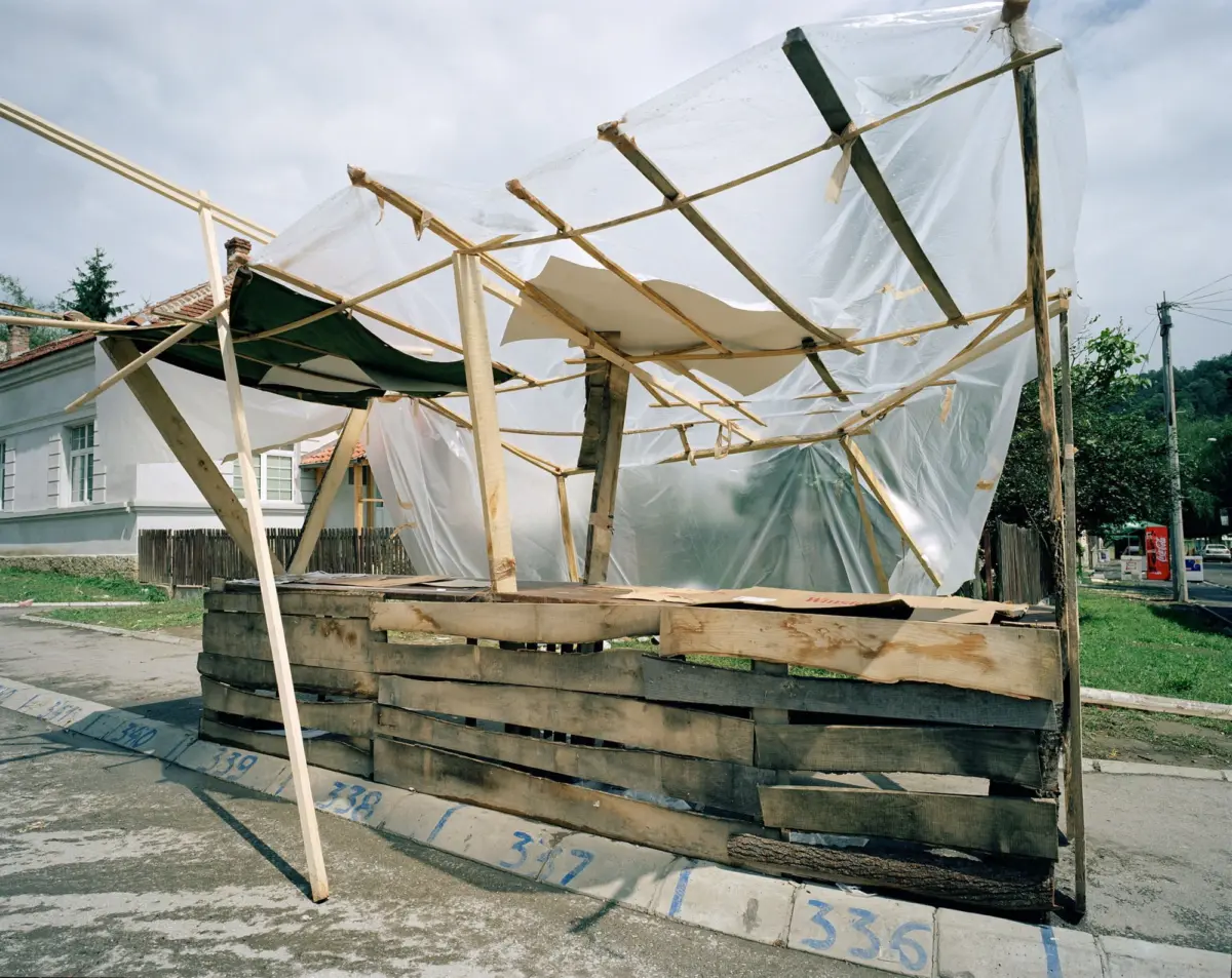 Wooden frame with torn translucent plastic sheets forms a makeshift shelter on a residential street.