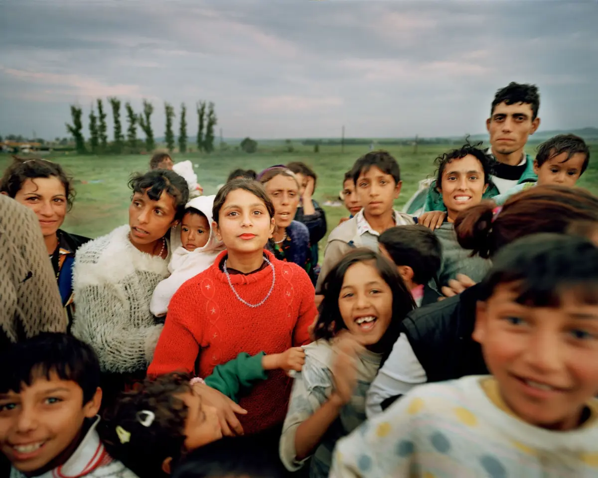 Group of smiling children outdoors in a field, posing for a photo under a cloudy sky.