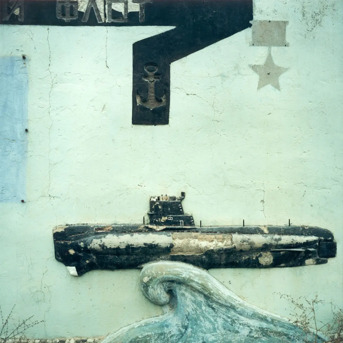 Weathered wall mural of a large black right-angle shape with an anchor symbol on its vertical leg and a faded star to the right.
